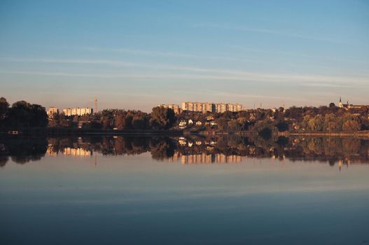 Orange sunset against the background of the river in September in the harvest season. Reflection in the water from the trees. Beautiful autumn landscape. Autumn colors are reflected in calm waters.