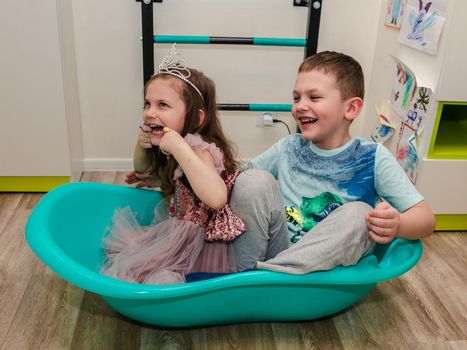 A boy and a girl have fun playing with a small bathroom in sailors, in the children's room of their house, brother and sister, close-up.