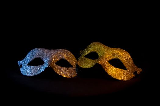 two shiny gold and silver carnival masks on black background