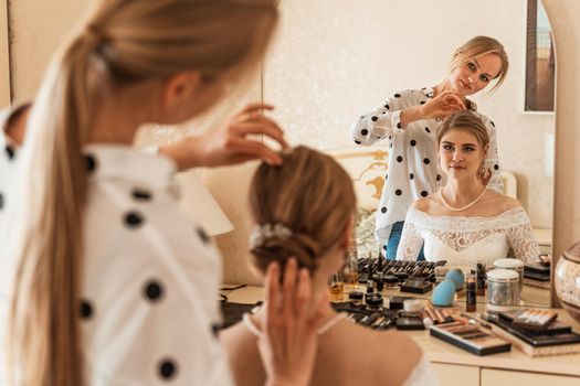 Make-up artist makes professional makeup for a young woman, a bride. The bride in a white dress, a pearl necklace and earrings. Make-up artist paints the bride's lips