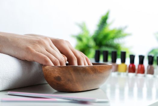 Closeup female hands in wooden bowl with water. Spa procedure and relaxation. Female hands preparing for manicure. Professional nail care and beautician service. Beauty and hygiene concept