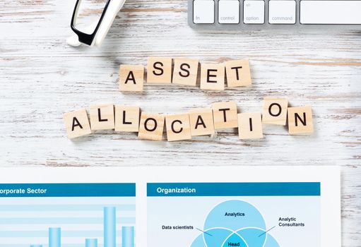 Asset allocation concept with letters on cubes. Still life of workplace with supplies. Flat lay vintage white wooden desk with computer keyboard and analytic report. Capital investment and management