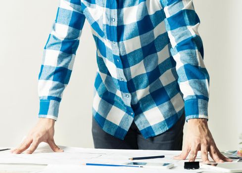 Architect standing near desk with paper blueprints. Architecture studio concept with design project. Close up man hand lying on construction drawing. Professional building, engineering and renovation