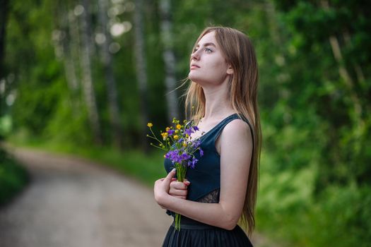 Portrait of a Russian girl with a bouquet of wild flowers in the evening at the village