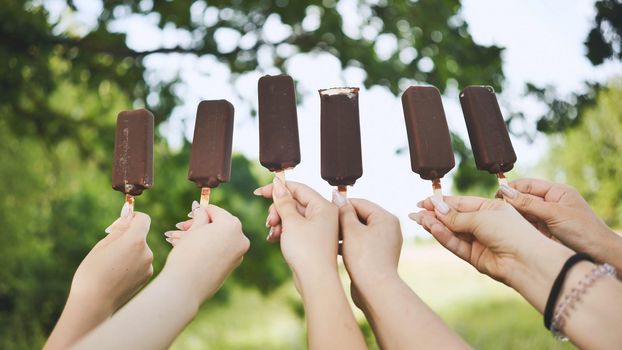 Friends hold chocolate ice cream on a stick in a row