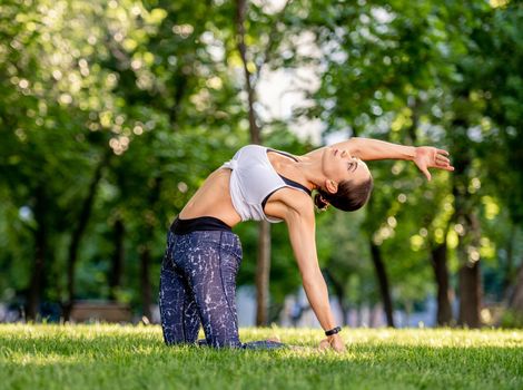 Sport girl doing yoga at nature and training her balance. Young woman exercising and stertching her body in summertime