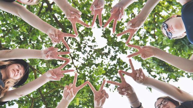 Girlfriends join fingers in a circle against the background of tree branches