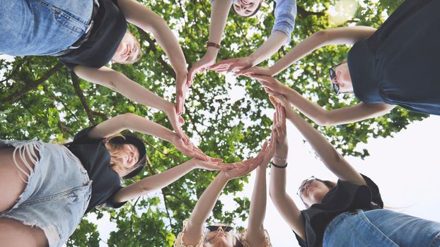 The girlfriends join their palms in a circle against the background of tree branches