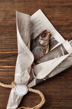 Salted air dried roach wrapped in newspaper like bouquet tied with coarse rope lying on rustic wooden surface. Concept of beer snack as gift for men