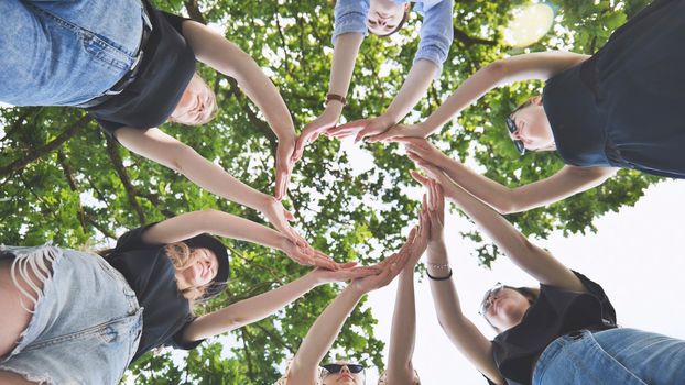 The girlfriends join their palms in a circle against the background of tree branches