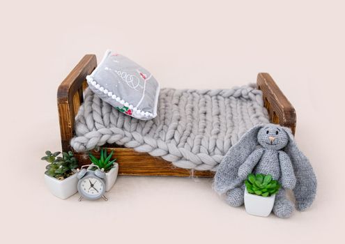 Newborn baby studio furniture tiny bed with fur decorated with flower plant and knitted bunny toy. Beautiful spot for infant child studio photoshoot