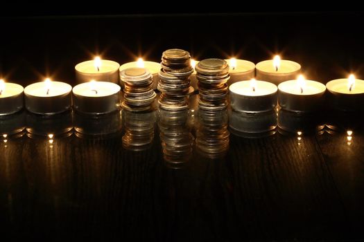 Set of coins between lighting candles on dark background