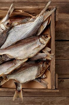 Closeup heap of salted air-dried roach in small crate on rough wooden background, cropped image