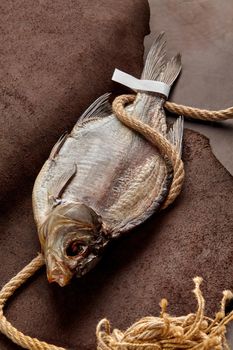 Whole salted dried roach wrapped in coarse rope with paper label on tail lying on brown genuine leather background