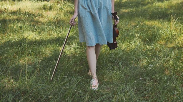 A girl in a dress walks with a violin in a city park