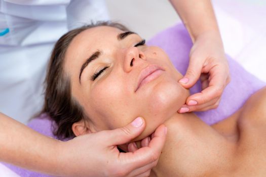 Relaxing massage. European woman getting facial massage in spa salon, side view.