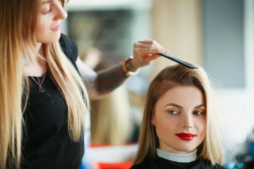 Portrait of hairdresser using comb to brush clients hair, woman on appointment in salon. Professional master in beauty center. Wellness, barbershop concept