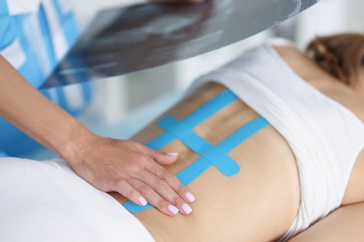 Close-up of woman doctor hold scan of woman back and correct kinesiology tape on females body. Treatment for faster recovery after injury. Health concept