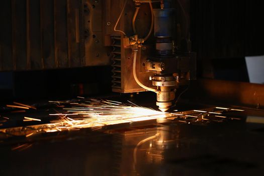 Close-up of sparks fly out of automated machine, metal processing laser on metallurgical background. Manufacturing, parts for automotive production concept