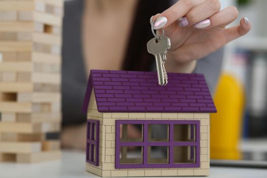 Close-up of female worker hand hold key to unlock new miniature toy house, buy new accommodation, invest in real estate. Agency, mortgage, realtor concept