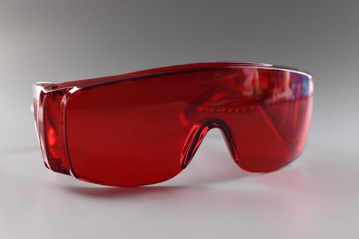 Close-up of red plastic safety glasses, protective workwear for human eyes. Reusable eyewear on grey surface. Occupational safety and eye health concept