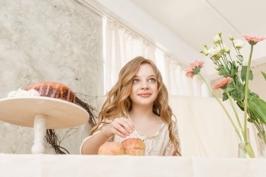 A girl with long hair in a light dress is sitting at the Easter table with cakes, spring flowers and quail eggs. Happy Easter celebration