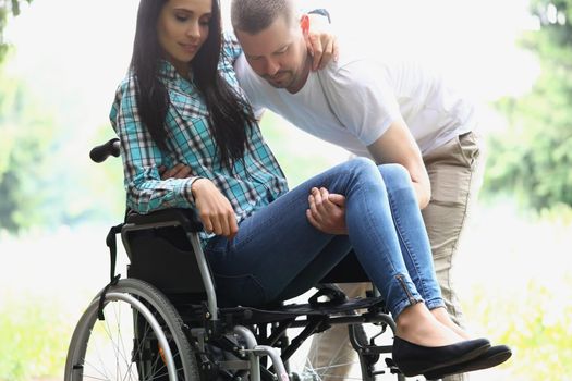 Portrait of man husband take woman in arms, disabled wife on wheelchair. Male partner visit in hospital. Disability, nursing house, care, recovery concept