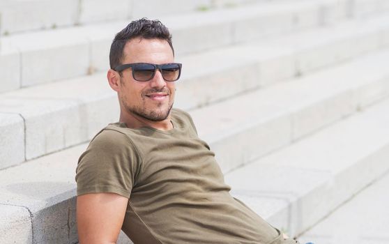 Male sitting alone on steps. Handsome boy with sunglasses