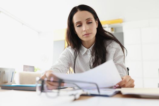 Portrait of tired overworked young woman go through paper on working place. Exhausted employee in office. Hardworker, businesswoman, workaholic concept