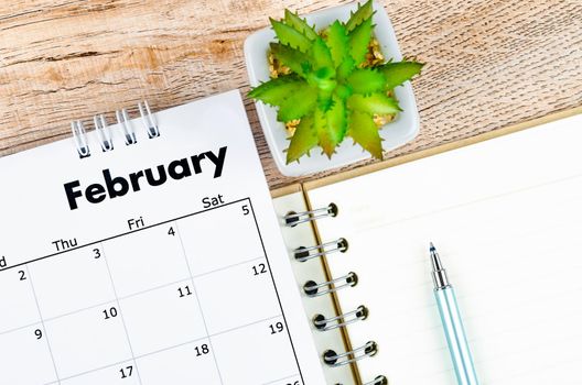 The February 2022 desk calendar and open diary with pen on wooden background.