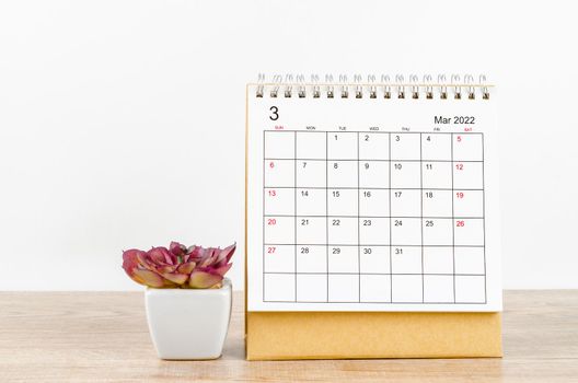 March 2022 desk calendar with plant pot on wooden table.