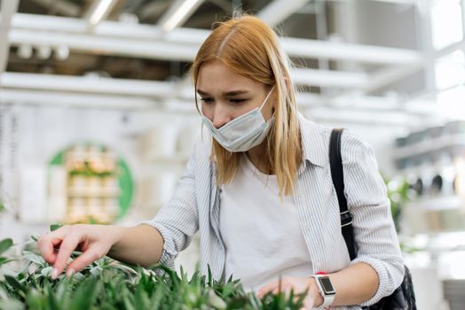 A young woman chooses home indoor plants in the store to create a cozy home.