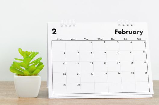 The February 2022 desk calendar with plant pot on wooden table.