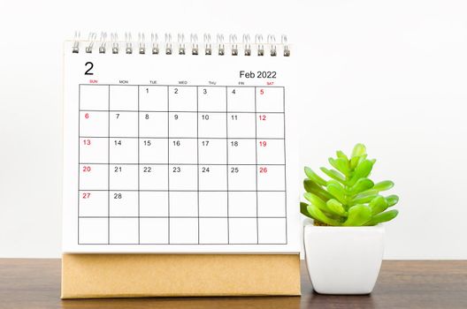 February 2022 desk calendar with plant pot on wooden table.