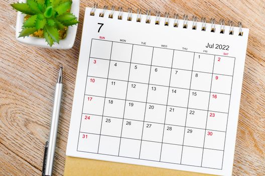 The July 2022 desk calendar with pen on wooden table.