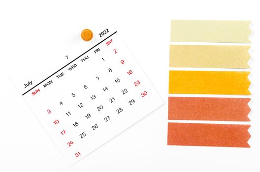 July 2022 calendar with wooden push pin and blank adhesive note paper on white background.