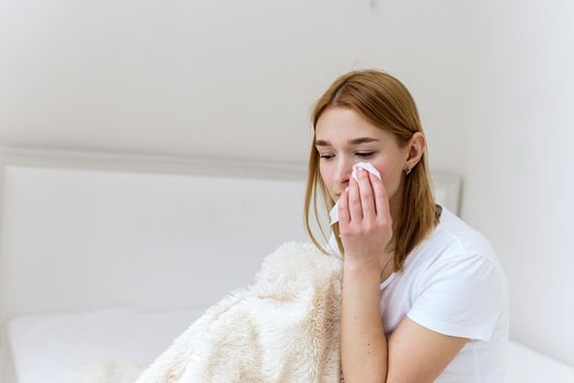 Unhappy depressed caucasian woman crying and wiping away her tears with a paper napkin, suffering from grief in the family. The woman is crying at home in her bed.