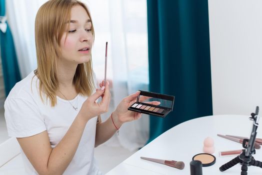 Beauty webinars, makeup classes online. Happy woman vlogger is showing cosmetics products while recording video stream on phone for her internet channel in social media. beauty blog about cosmetics and makeup.