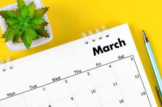 The March 2022 desk calendar and pen with plant pot on yellow background.