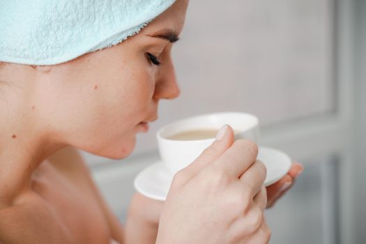 Young serene relaxed woman in spa bath towel drinking hot beverage tea coffee after taking shower bath at home. Beauty treatment, hydration concept