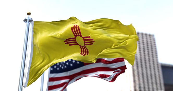 the flag of the US state of New Mexico waving in the wind with the American flag blurred in the background. New Mexico state flag It is one of four U.S. state flags not to contain the color blue