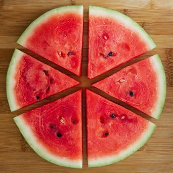 Slices of fresh red tasty watermelon laid out in a circle on a wooden background.