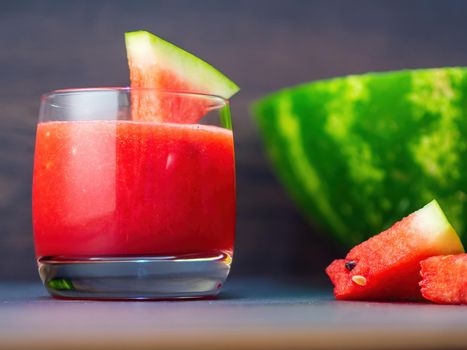 Fresh watermelon smoothie in a glass mug and slices of watermelon on a wooden background