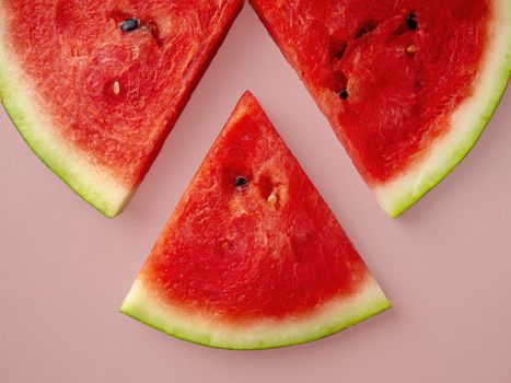 Slices of fresh red delicious watermelon are laid out in a circle on a colored background.