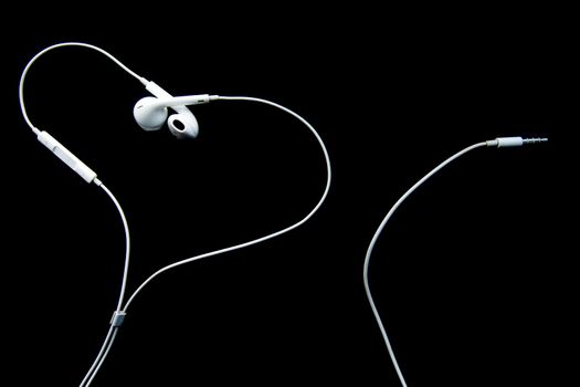 White wired headphones earbuds, headset in the shape of a heart on a black background. Music day