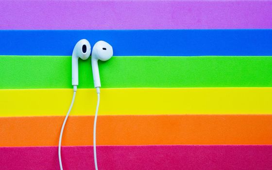 White wired headphones, headset on a multi-colored rainbow background (lgbt). Musical day