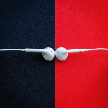 White wired headphones, headset on a black and red background. Musical day