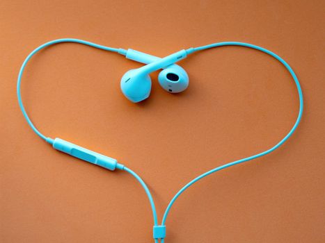 White wired headphones, headset in the shape of the heart on an orange background. Musical day
