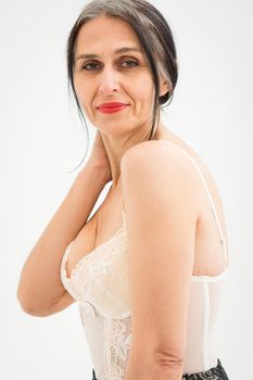 Middle aged woman starting getting grey-haired is posing in studio with naked shoulders on white background, face skin care beauty, middle age skincare cosmetics, cosmetology concept.