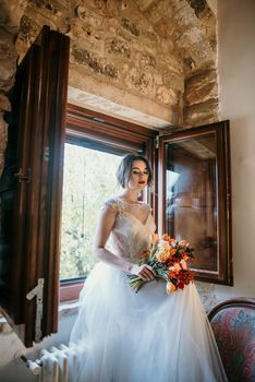 Artistic processing Fantasy girl princess in WHITE WEDDING dress stands in medieval CASTLE room looking vintage window. Bride in a luxury apartment in a wedding dress.. Sweet and gentle girl with fair skin alone in silence in an old castle, spirit of abandoned medieval building whirls in white smoke and magical thick fog in rays of sun